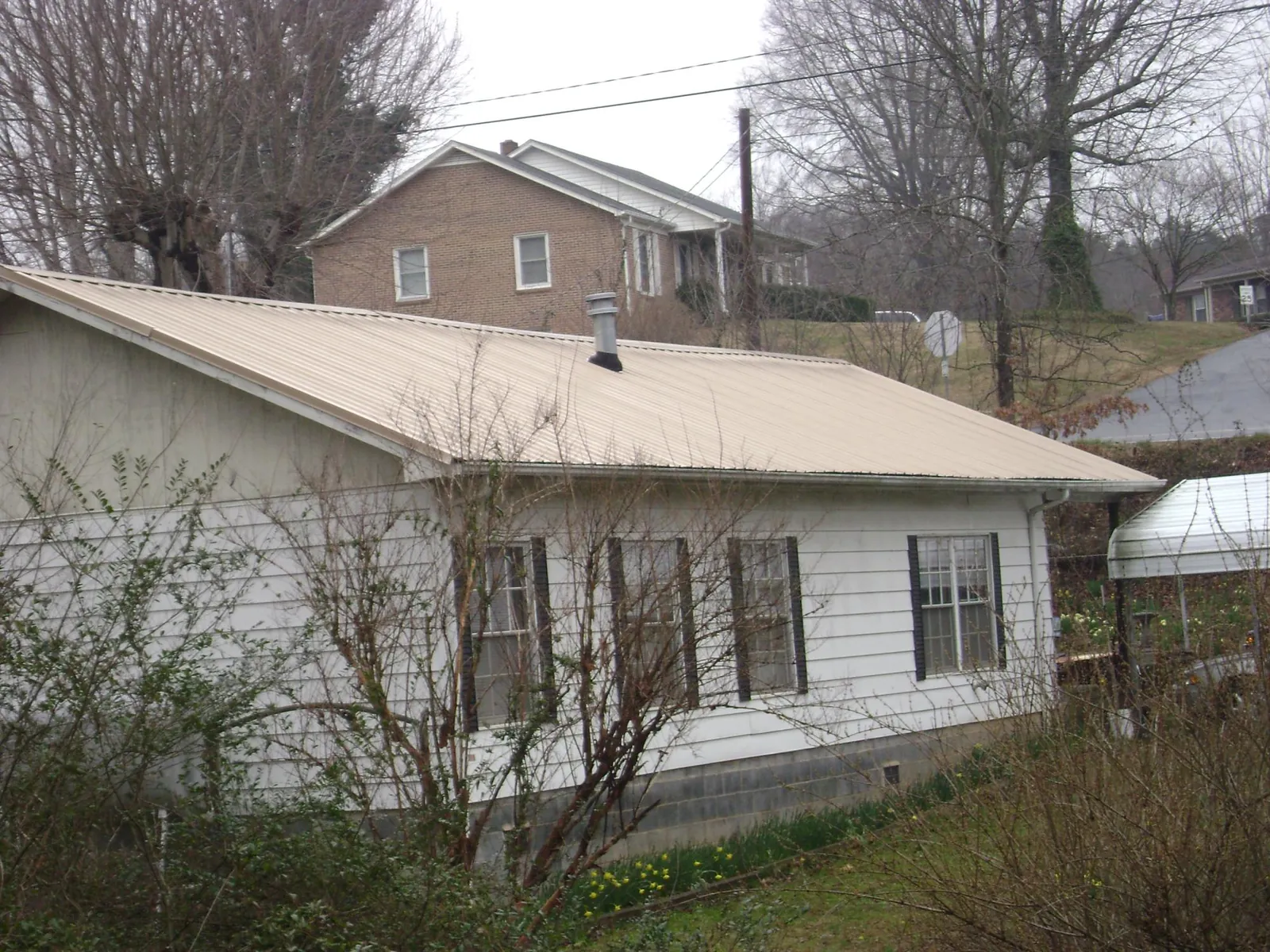 Tan metal roof on a white sided house set into a hillside — Commercial Roofing by Roofing Brothers in Epworth